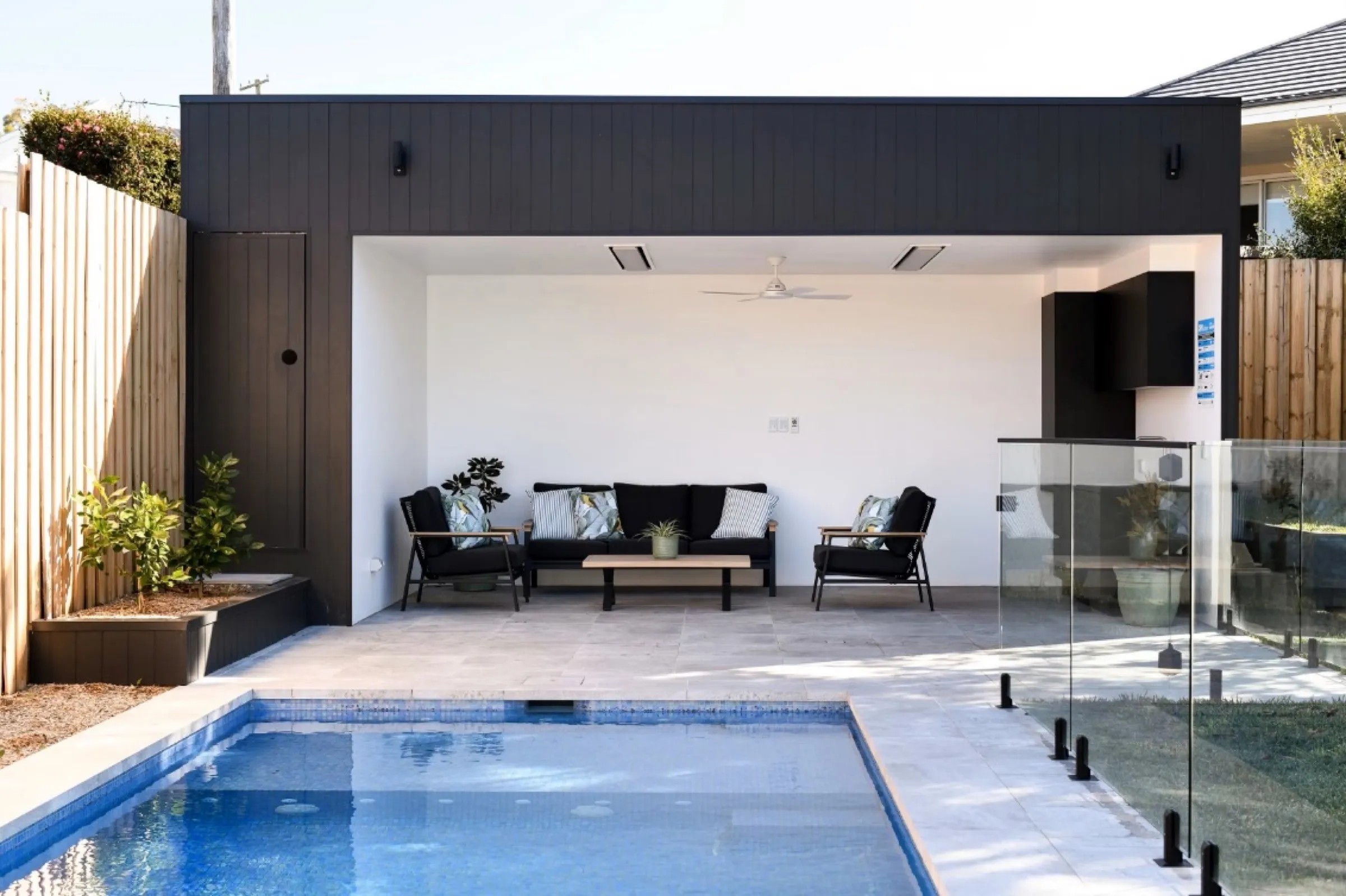 Dark clad pool cabana with an open lounge area beside a tiled pool
